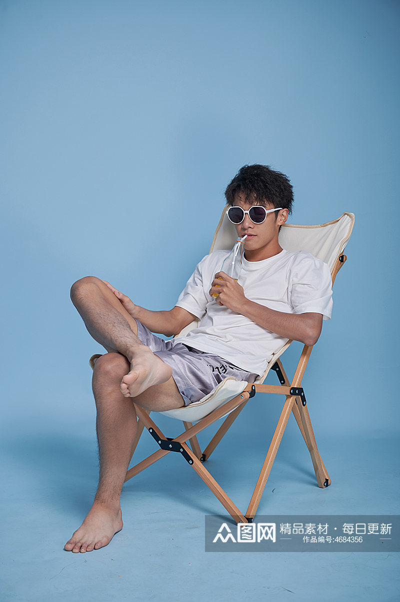 夏季男生喝饮料泳装坐沙滩椅摄影图素材