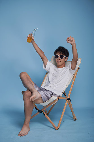 夏季男生喝饮料泳装坐沙滩椅摄影图