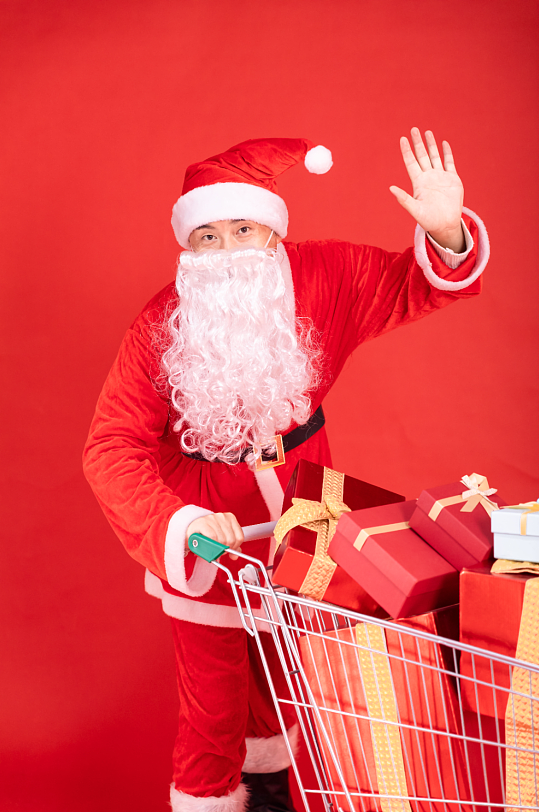 红色背景上推着购物车的圣诞老人摄影图