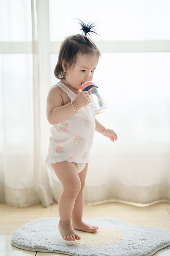 拿着奶瓶站着喝奶的婴幼儿摄影图
