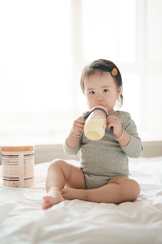 坐在床上喝奶粉的婴幼儿摄影图