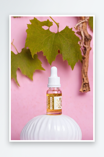 一瓶精油与金色颗粒附近葡萄叶子粉红色背景